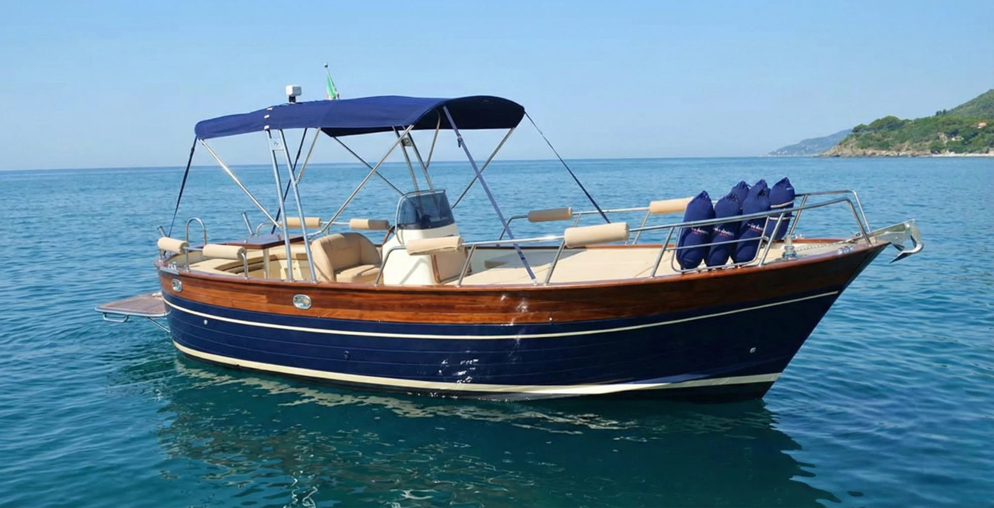 Gozzo blu con ponte in legno, divani imbottiti e tendalino.